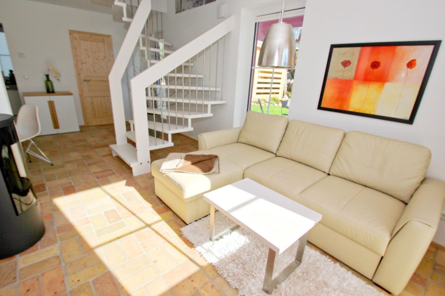 Una sala de estar con un sofá beige, una mesa de centro blanca, una escalera y un cuadro en la pared.