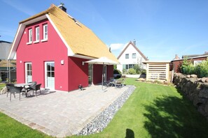 Ein rotes Haus mit Strohdach, einer Terrasse mit Gartenmöbeln und einem gepflegten Rasen.