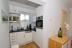 A modern kitchen with white cabinets, a black countertop, and stainless steel appliances. There is a wooden side table with a vase of flowers. - Falke Vacation Home - a stylish vacation home with a view of the sea, a terrace, and a fireplace - (Gager)