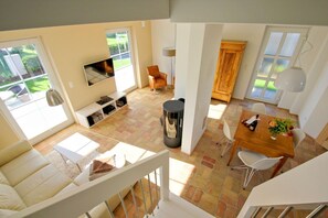 A spacious living area with a sofa, a TV mounted on the wall, a dining table with chairs, and a fireplace.
