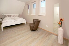 Une chambre à coucher avec un lit, un fauteuil marron, un miroir et un vase de fleurs.