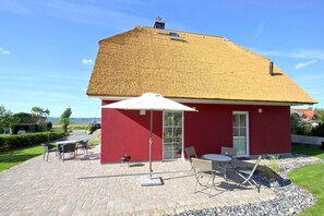 A red building with a thatched roof patio area, outdoor seating, and a view of the water.