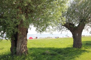 A grassy area with two large trees and a red tent in the background. - Vacation apartment close to the beach with a beautiful garden - Ferienhaus Gisela - Holiday home (Putbus)