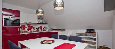 A modern kitchen with red cabinets, a white countertop, and two pendant lights.