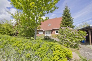 A house with a red roof, surrounded by a garden with various plants and flowers. - Vacation apartment close to the beach with a beautiful garden - Ferienhaus Gisela - Holiday home (Putbus)