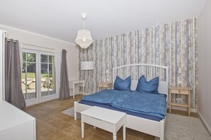 A bedroom with a bed, a desk, a chair, a lamp, and a view of the outdoors.