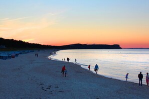 A beach with people walking along the shore, a clear sky, and a sunset.