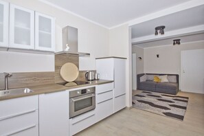 A modern kitchen with white cabinets, a wooden countertop, and a built-in oven. - Quiet location close to the sea, terrace and garden - Ferienhaus Auszeit FeWo 01 - (Middelhagen)