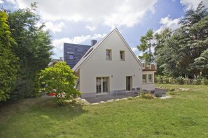 A two-story house with a sloped roof, a front porch, and a small garden area. - Quiet location near the sea, with a patio and garden - Ferienhaus Auszeit FeWo 01 - (Middelhagen)