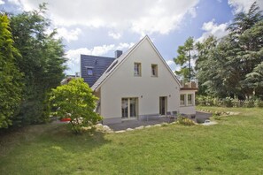A two-story house with a sloped roof, a front porch, and a small garden area.