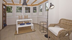 A room with a white table, chairs, a bookshelf, a wicker sofa, and a floor lamp. - Quiet location close to the sea, terrace and garden - Ferienhaus Auszeit FeWo 01 - (Middelhagen)