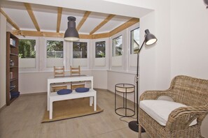 A room with a white table, chairs, a bookshelf, a wicker sofa, and a floor lamp. - Quiet location close to the sea, terrace and garden - Ferienhaus Auszeit FeWo 01 - (Middelhagen)