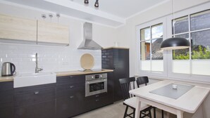 Una cocina moderna con encimera blanca, armarios oscuros, electrodomésticos de acero inoxidable y una zona de comedor con mesa y sillas blancas.