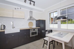 A modern kitchen with a white countertop, dark cabinetry, stainless steel appliances, and a dining area with a white table and chairs.