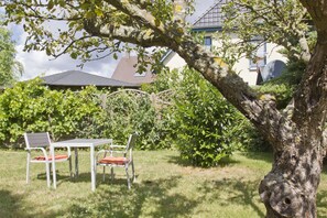 Ein Außenbereich mit Sitzgelegenheit, Tisch und Stühlen, umgeben von Pflanzen und einem Baum.