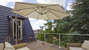 Una terraza con mobiliario de mimbre, un parasol grande y vista a árboles.