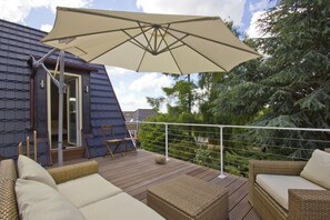 Eine Terrasse mit Korbmöbeln, einem großen Sonnenschirm und Blick auf Bäume.