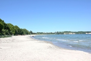 Ein Strand mit sandigem Ufer, ruhigem Wasser und blauem Himmel.