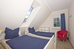 Ein Schlafzimmer mit zwei Betten, einem Oberlicht, einem Fenster mit Vorhängen und einem roten Sessel.