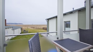 Un balcon donnant sur un champ verdoyant et un bâtiment. On y trouve deux chaises et une table.