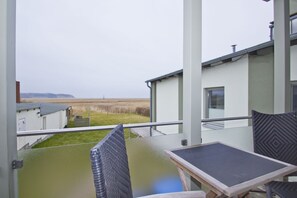 Un balcón con vista a un campo cubierto de hierba y un edificio. Hay dos sillas y una mesa en el balcón.