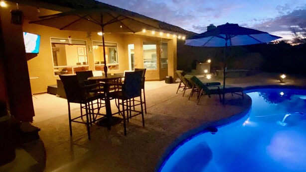 Un patio exterior con piscina, mesa de comedor, sillas y sombrillas.