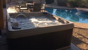 Un jacuzzi con chorros de agua, una piscina, mobiliario de patio y sombrillas.