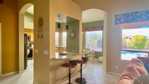 Amplia sala de estar con cocina, comedor con taburetes de bar y vista a una piscina.