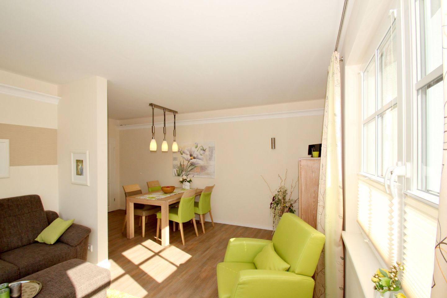 A living room with a brown sofa, a green armchair, a wooden dining table, and a chandelier.