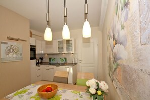 Una cocina moderna con armarios blancos, una mesa de madera y un cuadro en la pared.
