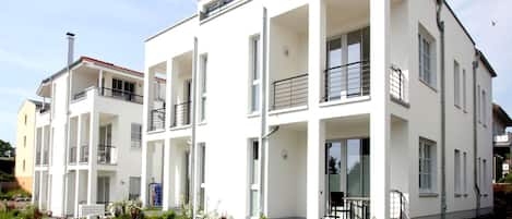 Un moderno edificio residencial de varios pisos con balcones, ventanas amplias y un jardín bien cuidado.
