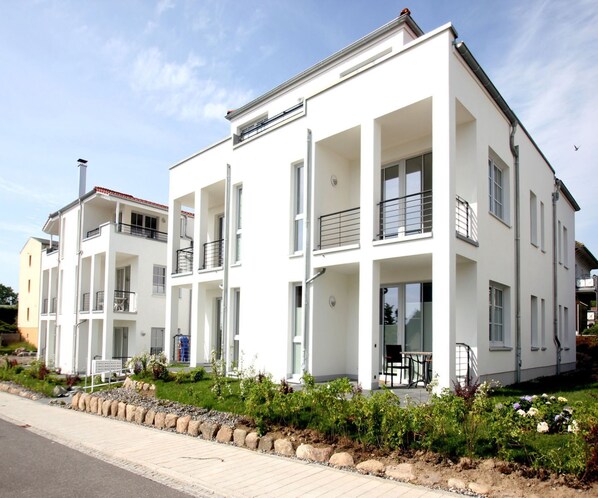 A modern multi-story residential building with balconies, large windows, and a well-maintained garden area.