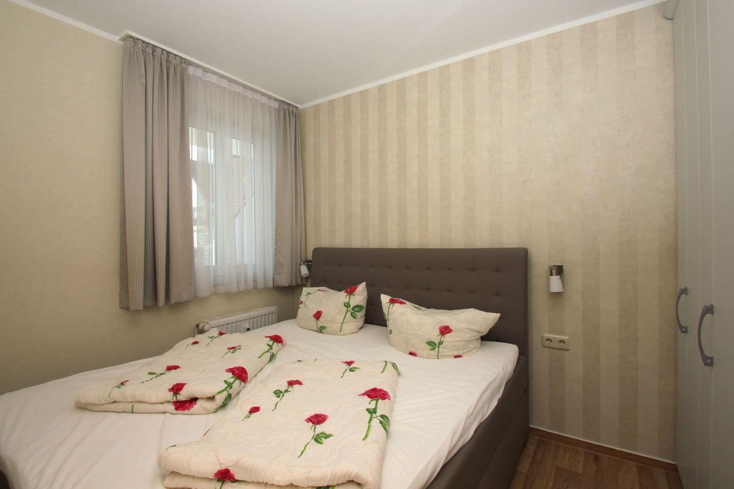 Une chambre à coucher avec un lit, des rideaux, un radiateur et une lampe fixée au mur.