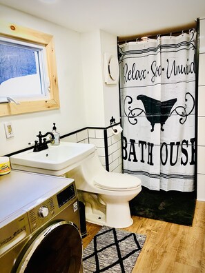 A bathroom with a bathtub, a sink, a toilet, and a washing machine. - Charming 120-year-old farmhouse by the creek (Hancock)