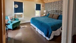 Un dormitorio con techo de madera, una cama con colcha azul, una silla y una ventana con vistas al exterior.