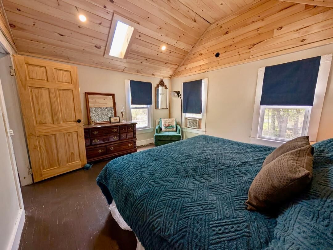 Ein Schlafzimmer mit Holzboden, einem Bett mit gemustertem Überwurf, einem Schminktisch, einem Stuhl und einem Fenster mit Blick.