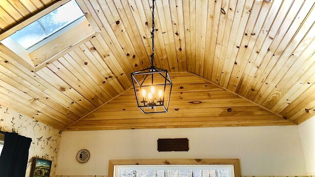 Una habitación con vigas de madera en el techo, tragaluces, un cuadro enmarco y una ventana con vistas a un bosque nevado.