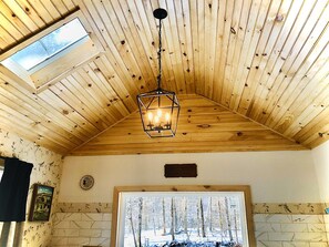 A room with wooden ceiling beams, a skylight, a framed picture, and a window with a snowy forest view. - Charming 120-year-old farmhouse by the creek (Hancock)
