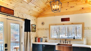 Una cocina moderna con techo de madera, un ventanal con vistas a un bosque y un cartel que dice "BELIEVE".