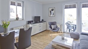 A modern living room with a sofa, chairs, a coffee table, a TV, and a dining area with a table and chairs.