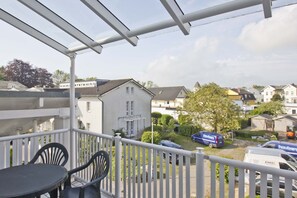 A balcony with a table and chairs, overlooking a residential area with houses and parked vehicles.