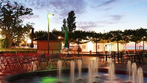 An outdoor seating area with chairs and tables, a fountain, and a building in the background.