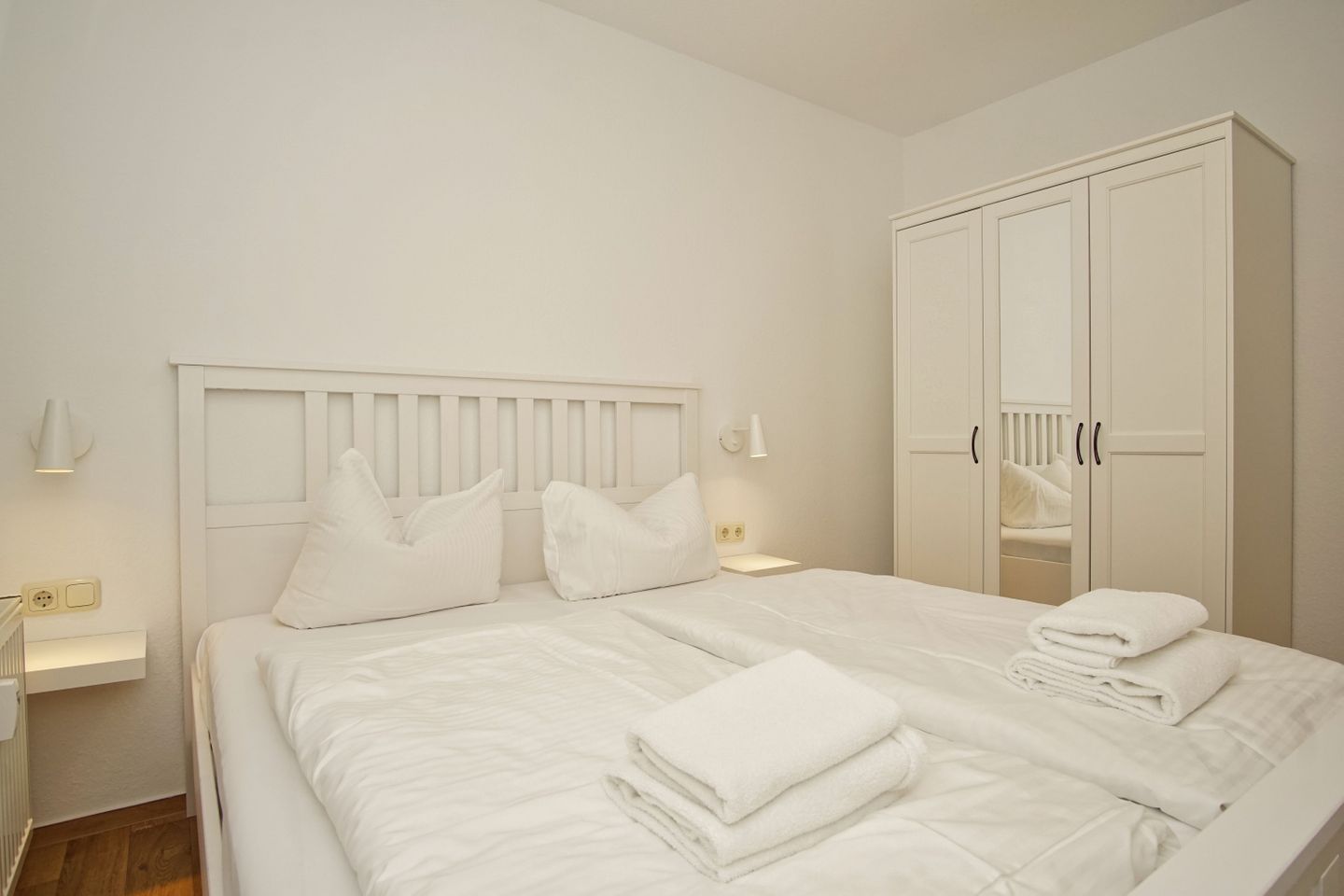 A neatly made bed with pillows, a bedside lamp, and a wardrobe with a mirror.
