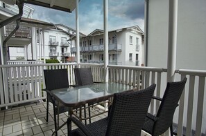 A balcony with a glass table and wicker chairs, overlooking a row of white buildings with balconies. - Centrally located vacation apartment with balcony - Villa Karola FeWo 13 - Villa Karola (Göhren)
