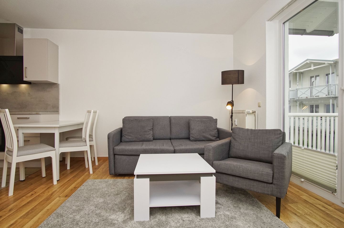 A modern living room with a grey sofa, white coffee table, and a dining area with white chairs and a table.