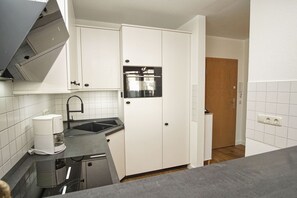 A compact kitchen with white cabinets, a black countertop, a coffee maker, and a built-in oven. - Balcony, free use of the AHOI adventure pool and sauna - Villa Karola FeWo 09 - (Göhren)