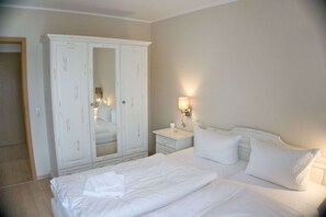 A hotel room with a large white wardrobe, a bed with white linens, a bedside table with a lamp, and a nightstand. - Centrally Located Vacation Apartment with a Balcony - Villa Karola FeWo 18 - Villa (Göhren)