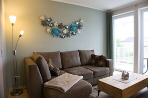 A living room with a brown sofa, a coffee table, and a wall decoration of fish. - Centrally Located Vacation Apartment with a Balcony - Villa Karola FeWo 18 - Villa (Göhren)