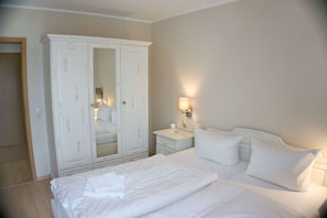 Ein Hotelzimmer mit einem großen weißen Kleiderschrank, einem Bett mit weißer Bettwäsche, einem Nachttisch mit Lampe und einem kleinen Tisch am Bett.