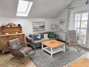 A cozy living room with a sofa, two chairs, a wooden coffee table, a fireplace, and a large window.